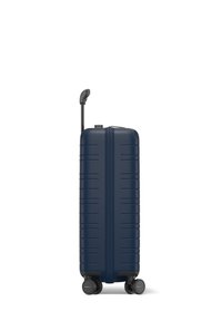 Valise rigide navy avec des rainures verticales, une poignée rétractable et quatre roues noires pour la mobilité. Texture lisse et design épuré.