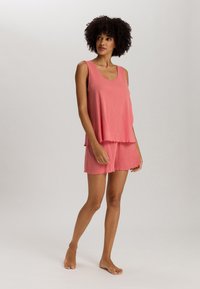 Top sin mangas de color rosa con un diseño en capas y un dobladillo en forma de concha, combinado con pantalones cortos a juego que presentan un acabado texturizado similar.