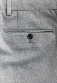Gray fabric trousers detail showing back pocket with black button and belt loop above.