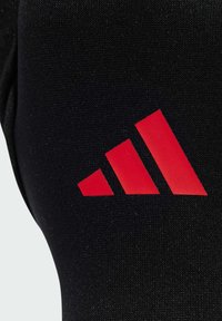 Tessuto nero con una trama liscia che mostra un prominente logo adidas rosso composto da tre strisce diagonali.