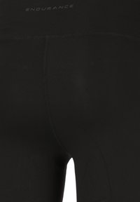 Svarta träningstights i stretchmaterial, med en slät yta och en söm över ryggen, märkta med "ENDURANCE" på midjebandet.