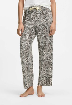 Personne portant un pantalon ample à imprimé léopard avec une taille à cordon et debout pieds nus sur fond blanc.