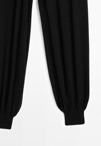 Schwarze, gestrickte Hose mit lockerem Schnitt und elastischen Bündchen. Glatte Textur und voluminöse Beine, die zu den Knöcheln hin schmal zulaufen.