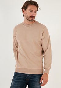 Felpa beige a girocollo realizzata in tessuto testurizzato, con orlo e polsini a coste, indossata con jeans scuri. Dettaglio della cucitura sulle spalle visibile.