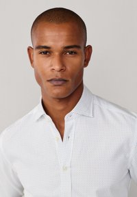 Witte button-up blouse met een subtiel blauw stippenpatroon. Kenmerkt zich door een omgeklapte kraag en een enkele borstzak. Gladde textuur.