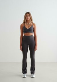 Ensemble de sport gris comprenant un bralette ajusté avec de fines bretelles et un legging taille haute. Tissu lisse avec un léger éclat, associé à des baskets blanches.