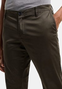 Pantaloni in cotone verde scuro con una texture liscia, dotati di chiusura con bottone, tasche laterali e design slim-fit.