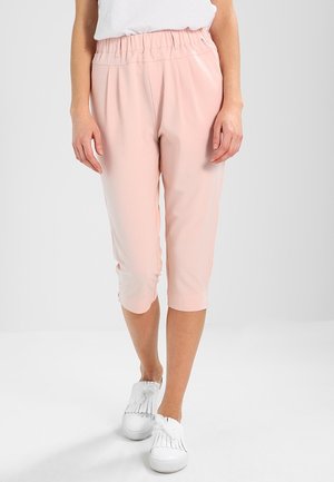 Pantalons courts rose clair avec une taille élastique et une texture lisse, associés à des chaussures blanches avec des franges.