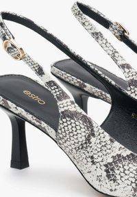 Czarne i białe buty na obcasie typu slingback z wężowej skóry, z ostro zakończonym noskiem i złotymi akcentami.