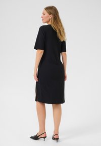 Robe midi noire côtelée avec des manches courtes, fentes latérales et une coupe décontractée. Stylisée avec des talons noirs à enfiler. Texture lisse.