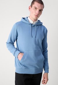 Moleton azul claro feito de tecido macio, com um bolso frontal, capuz ajustável por cordão e um pequeno logotipo no peito.