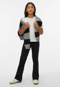 Stickad grå och svart randig cardigan hängd över en vit t-shirt, kombinerad med svarta utsvängda jeans och vita sneakers med beige detaljer.