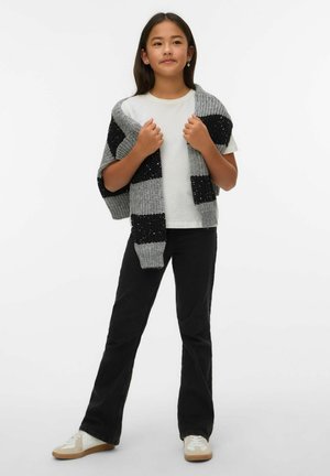 Cardigan rayé gris et noir en tricot, posé sur un t-shirt blanc, associé à un jean évasé noir et des baskets blanches avec des accents beige.