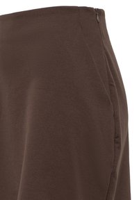 Gros plan d'une jupe en tissu marron montrant une fermeture éclair latérale et une texture lisse avec des détails de couture subtils.