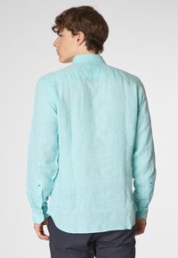 Camicia di lino azzurro chiaro con maniche lunghe, colletto a punta e polsini abbottonati. Presenta una finitura testurizzata e una vestibilità rilassata con orlo curvo.