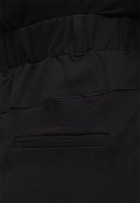 Pantalons de jogging noirs avec une taille texturée, dotés d'une ceinture lisse et d'un petit détail de poche à l'arrière. Le tissu semble doux et extensible.