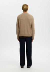 Beige Strickpullover mit weicher Textur und geripptem Saum, kombiniert mit dunkelblauen weiten Hosen, Ansicht von hinten.