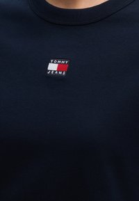 Chemise bleu marine avec petit logo Tommy Jeans comprenant des drapeaux blancs et rouges brodés sur la poitrine.