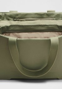 Olive zöld vászontáska texturált külső résszel, felső cipzáras záródással és belső cipzáras zsebbel. Masszív, bordázott fogantyúkkal rendelkezik.