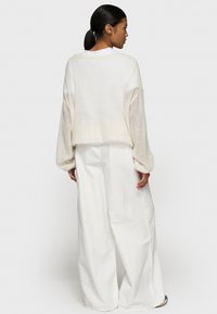Maglione a maglia crema con maniche a palloncino, design leggermente corto, abbinato a pantaloni bianchi a gamba larga a vita alta. Texture liscia.
