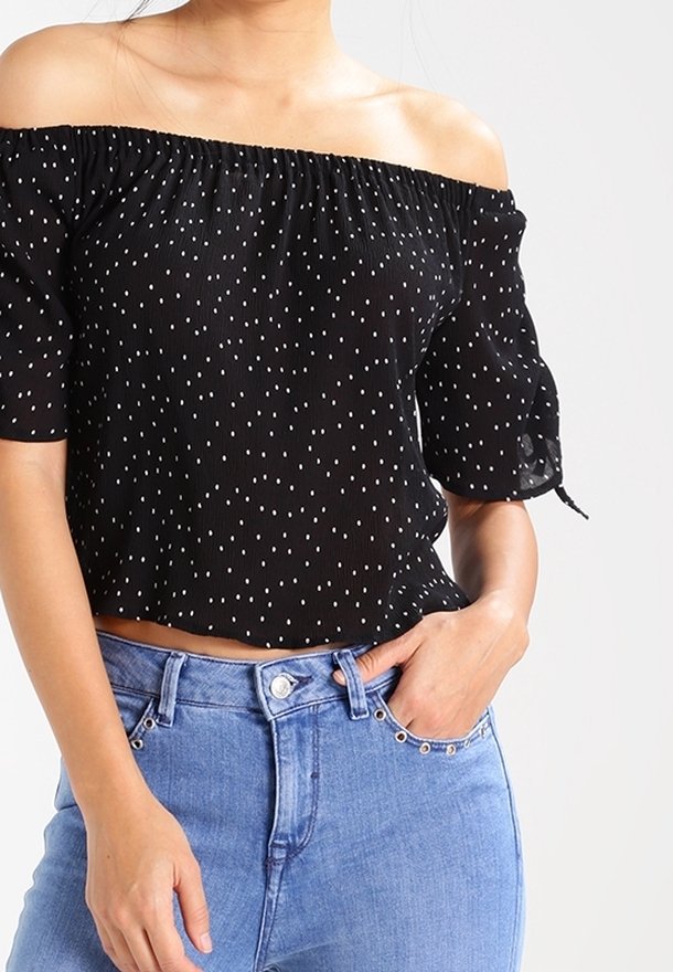 Schwarzes Off-Shoulder-Oberteil mit weißen Polka Dots, kurzen Puffärmeln und gerafftem Halsausschnitt, kombiniert mit hochgeschnittenen blauen Jeans.