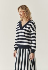 Felpa a righe in navy e bianco, con scollo a V e maniche lunghe. Abbinata a una gonna a righe coordinata per un look intonato.