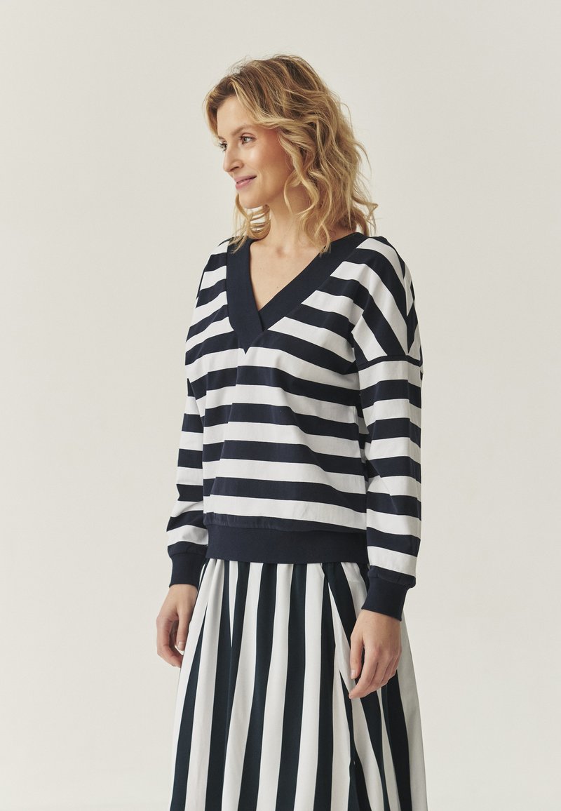 Felpa a righe in navy e bianco, con scollo a V e maniche lunghe. Abbinata a una gonna a righe coordinata per un look intonato.
