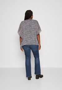 Blusa leggera a fantasia floreale con un design leggero; abbinata a jeans a zampa d'elefante blu e stivali neri con tacco.