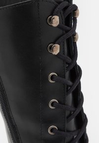 Stivale in pelle nera con occhielli metallici, dotato di lacci neri, cerniera laterale e superficie liscia.