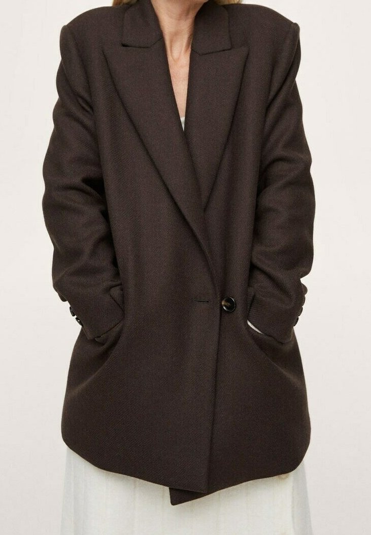 Dark brown blazer with a textured fabric, oversized shape, sharp lapels, single button closure, and side pockets. Smooth and structured design.