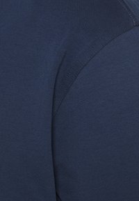 Marinblå bomullströja med en slät yta, med rund halsringning och korta ärmar, visad från axelperspektiv.