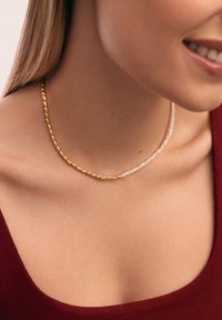 Collana di perle dorate e bianche con ovali dorati alternati a piccole perle bianche, progettata in uno stile delicato e stratificato.