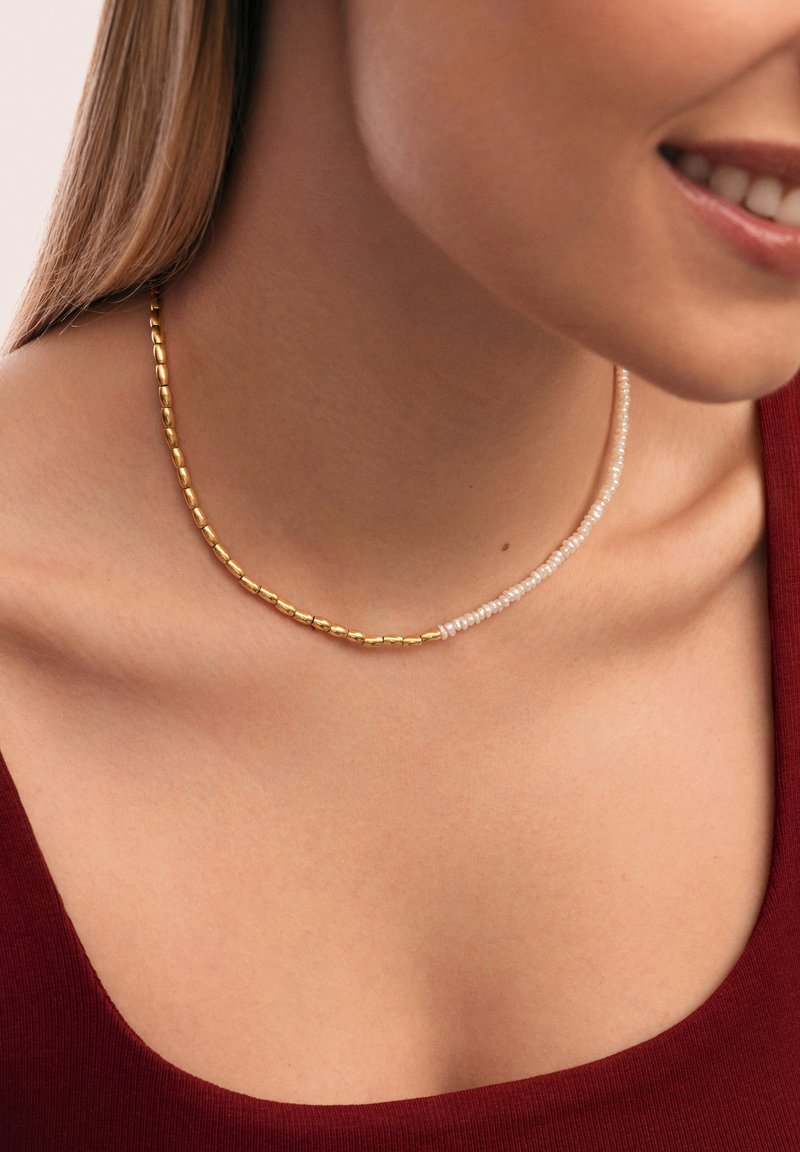 Collana di perle dorate e bianche con ovali dorati alternati a piccole perle bianche, progettata in uno stile delicato e stratificato.