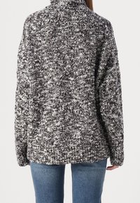 Pletený svetr v černobílém melírovaném vzoru, s vysokým límcem a oversized střihem. Měkká textura s kleslými ramenními švy.