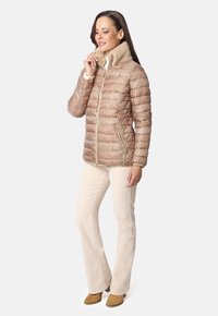 Chaqueta de plumas marrón con estampado y un suave collar de piel sintética beige, dos bolsillos con cremallera y cierre frontal con cremallera. Combinada con pantalones acampanados beige.