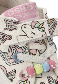 Zapatillas de lona con un estampado de unicornio en colores pastel, cordones grises y cuentas decorativas de colores en los cordones. La etiqueta rosa dice "Osito Conguitos."