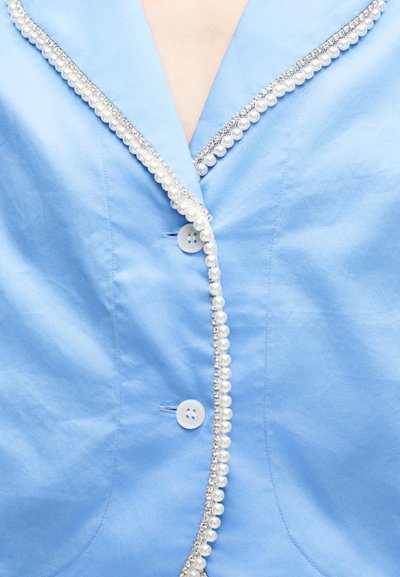 Ανοιχτόχρομο γαλάζιο ένδυμα με κουμπιά και V-λαιμόκοψη, διακοσμημένο με κορδέλα από λευκές πέρλες και μικρά διαυγή κρύσταλλα κατά μήκος των ακμών.