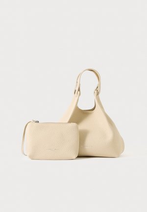 Beige strukturierte Lederhandtasche mit kurzen Griffen und passendem kleinen Reißverschlusstäschchen neben ihr auf hellem, einfarbigem Hintergrund.