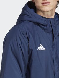 Námořnická modrá bunda adidas s kapucí, se zipem a bílým logem na levém prsu, hladká textura a nestrukturovaný design.