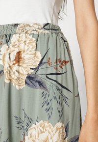 Falda floral con fondo verde, decorada con grandes flores beige y azul oscuro, cintura elástica y tejido ligero.