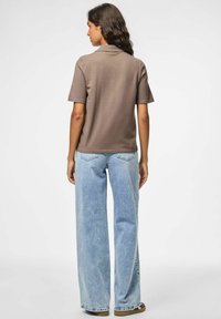 Brun kortärmad polo tröja med rak passform, i kombination med ljusblå vida jeans. Har en klassisk krage och enkel tygtextur.