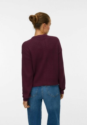 Pull en tricot épais de couleur baie avec un design texturé, col rond et coupe décontractée, associé à un jean bleu taille haute.