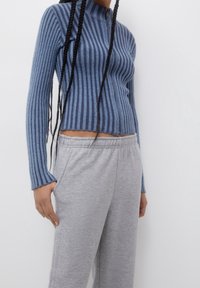 Blauw ribgebreid top met een hoge kraag en rits, gecombineerd met grijze katoenen sweatpants. De top heeft verticale strepen en een aansluitend ontwerp.