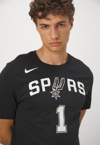 Sort bomulds t-shirt med "SPURS" i hvid, et sølvfarvet grafik med en stjerne, og nummeret "1" i grå med en perforeret tekstur. Nike-logo på ærmet.
