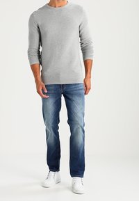 Suéter de punto texturizado gris, jeans azules desgastados y zapatillas blancas. El conjunto cuenta con mangas largas y un diseño de cuello redondo.