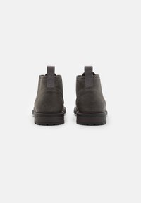 Bottines gris foncé avec une tige en cuir lisse, des languettes à l'arrière et des semelles en caoutchouc texturé. Présente des détails de couture contrastés.