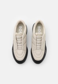 Beige sneakers med strukturerad ovandel, med vadderade paneler och svart gummisula. Varumärkeslogotypen "BOSS" i vitt på tungan och innersulorna.