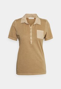 Kortärmad beige polo-shirt med kontrastkrage, knappslå och bröstficka mot en enkel vit bakgrund.