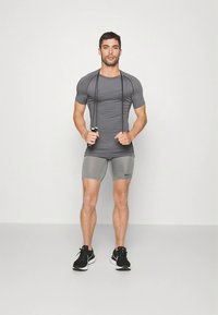 Abbigliamento sportivo composto da una maglietta aderente a maniche corte grigia e da pantaloncini grigi. L'outfit include un logo nero e scarpe da allenamento nere.