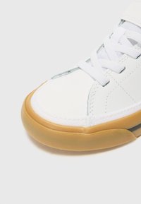 Vit sneaker med en texturerad ovandel i syntetläder och textil, en gummisula i färgen gum och vita snören.